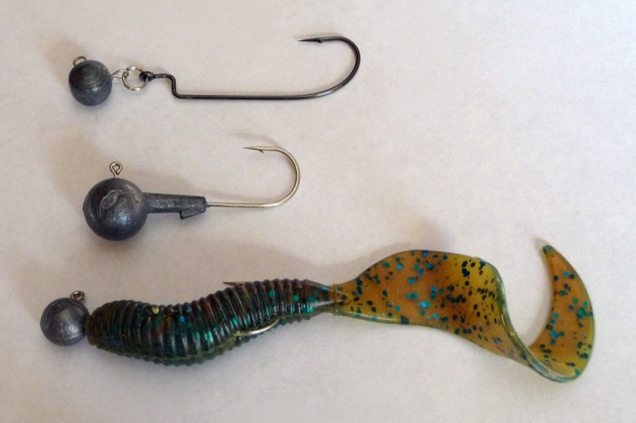 Two bare lead jig heads and a third rigged with a green curly-tail plastic body.