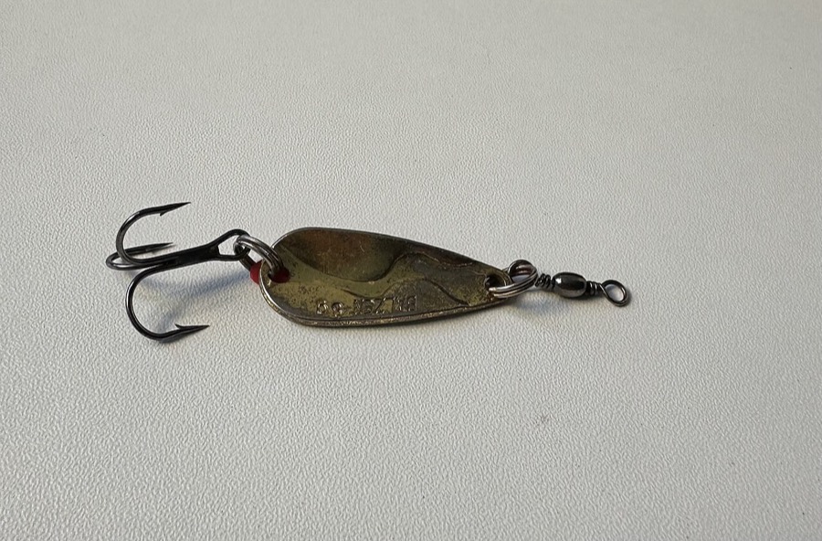 A curved metal casting spoon with a single treble hook.
